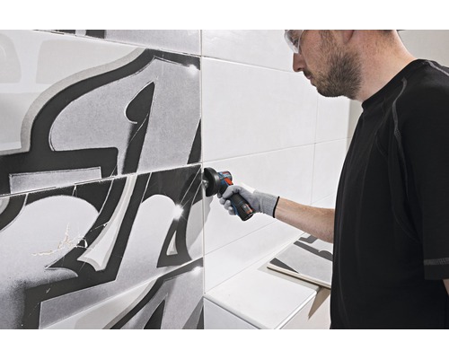 Handwerker bearbeitet Fliesen mit einem Winkelschleifer in einem Badezimmer.
