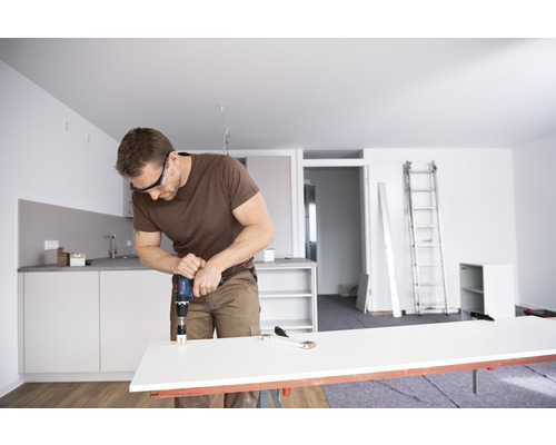 Mann bohrt Loch in Arbeitsplatte mit Bohrmaschine in heller Wohnung