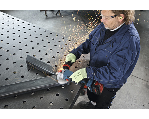 Mann schleift Metall mit einem Winkelschleifer auf einem Arbeitstisch, wobei Funken entstehen.