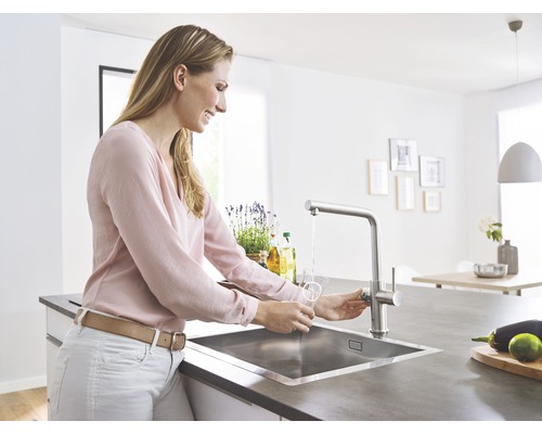 Frau füllt Wasser in ein Glas am Spültisch mit einer Armatur in einer hellen Küche.