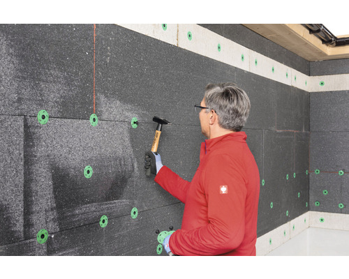 Mann befestigt Dämmplatten mit Hammer an der Wand