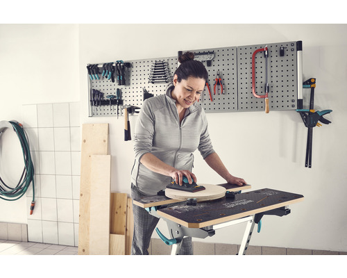 Frau schleift Holz auf einer Werkbank mit Werkzeugen an einer Lochwand