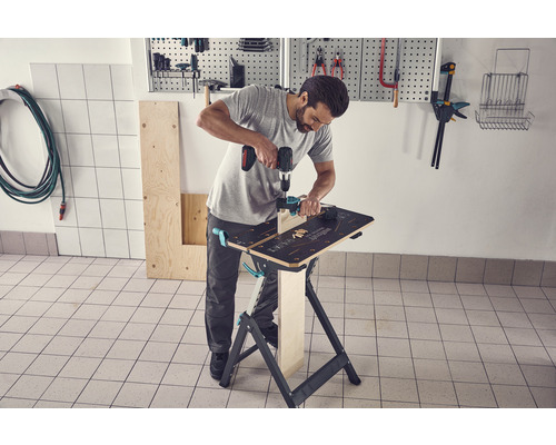 Mann arbeitet mit einer Bohrmaschine an einer Werkbank in einer Werkstatt.