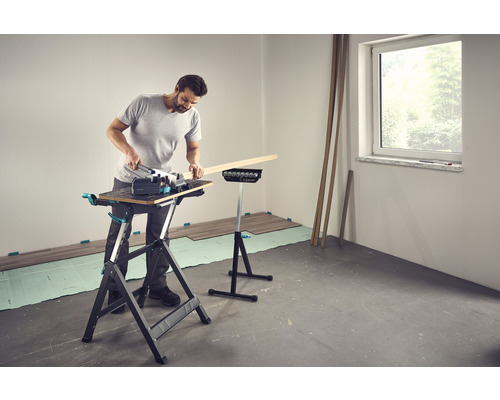 Mann arbeitet mit einer Stichsäge auf einer Werkbank in einem Raum mit Laminatboden.