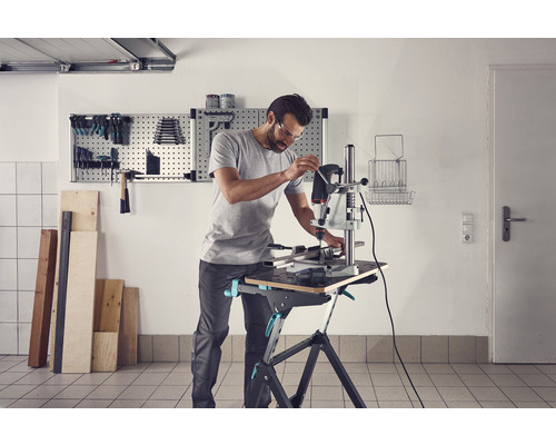 Mann arbeitet mit einer Tischbohrmaschine auf einer Werkbank in einer Werkstatt.