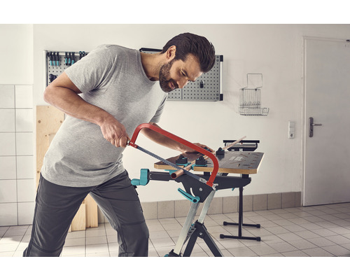 Ein Mann sägt ein Rohr auf einer Werkbank mit einer Metallsäge.