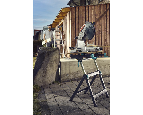 Gehrungssäge auf einem Sägetisch im Außenbereich mit einer Person auf einer Leiter