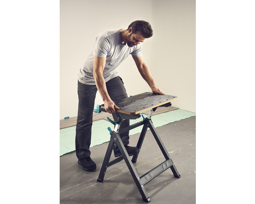 Mann arbeitet an einer Werkbank. Die Werkbank hat eine Arbeitsfläche mit Löchern und ein A-förmiges Gestell.