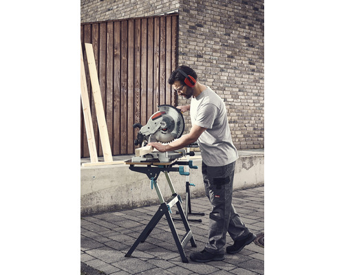 Mann sägt Holz mit einer Kappsäge auf einem Arbeitstisch im Freien.