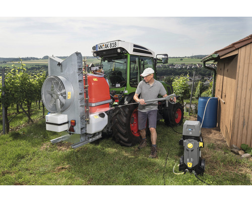 Ein Mann reinigt einen Traktor mit einem Hochdruckreiniger in einer ländlichen Umgebung.