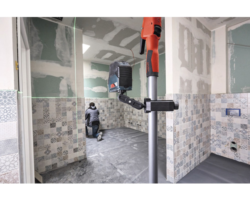 Ein Arbeiter verwendet ein Linienlaser-Nivelliergerät mit Stativ in einem Badezimmer mit Fliesen.