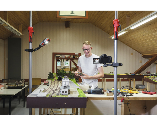 Mann filmt eine Modelleisenbahn mit einer Kamera auf einem Stativ und einer Arbeitsleuchte.