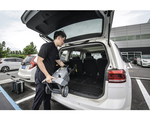 Eine Person verlädt einen mobilen Hochdruckreiniger in den Kofferraum eines Autos.