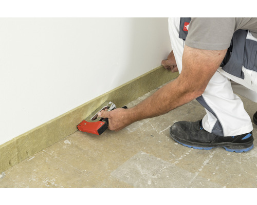 Ein Arbeiter befestigt eine Sockelleiste mit einem Tacker an einer Wand.