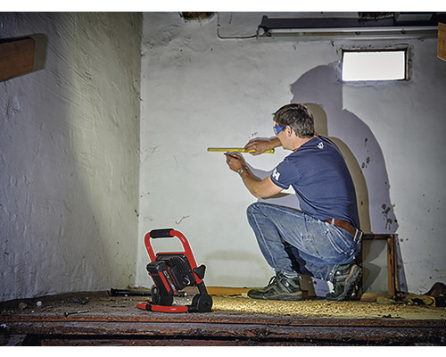 Mann misst Wand mit Zollstock, Baustrahler leuchtet im Raum
