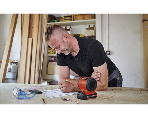 Ein Mann arbeitet an einem Bauplan mit einer Einhell Akku-Lampe auf dem Tisch.