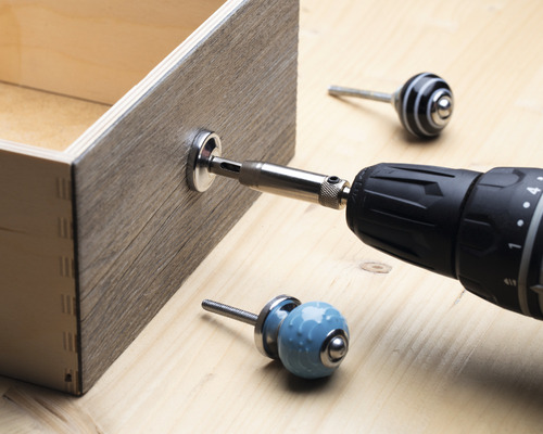 Eine Schublade wird mit einem Akkubohrer und einem Möbelknopf montiert.