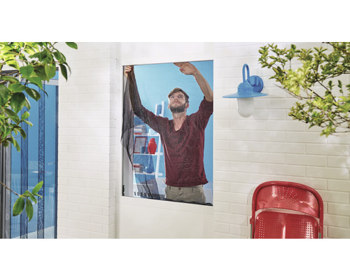 Ein Mann befestigt ein Insektenschutzgitter an einem Fensterrahmen.