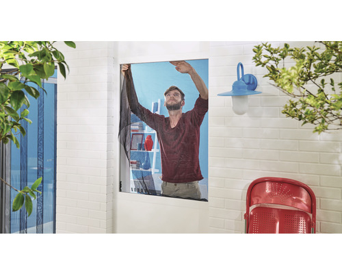 Mann montiert ein Insektenschutzgitter an einem Fenster.