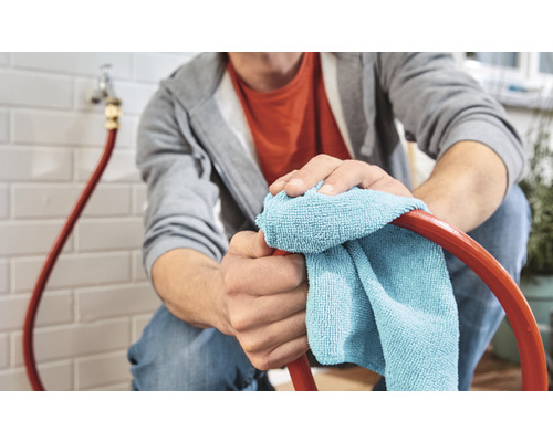 Eine Person reinigt einen Schlauch mit einem Tuch in einem Haus.