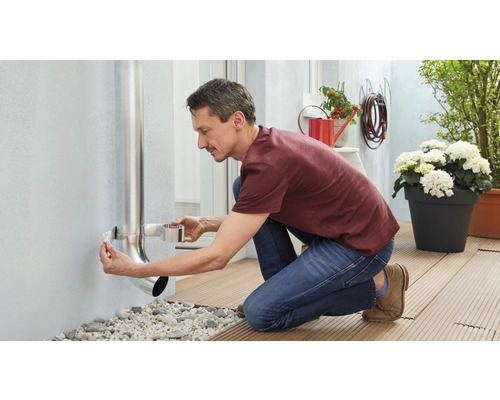 Mann befestigt ein Regenrohr mit Dichtband an einer Hauswand.