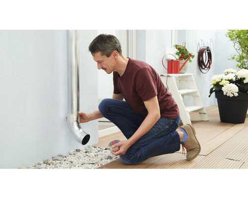 Ein Mann befestigt ein Regenrohr an einer Hauswand im Außenbereich.