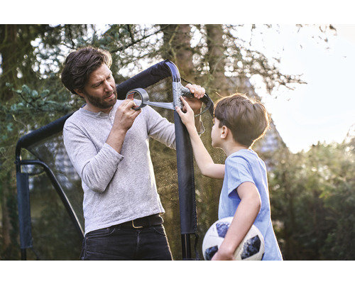 Vater und Sohn reparieren ein Fußballtor mit Klebeband im Garten.