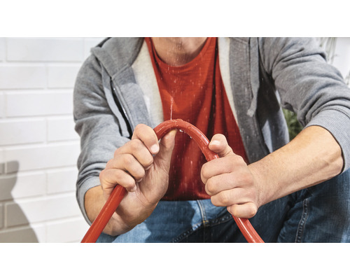 Eine Person hält einen undichten Gartenschlauch.