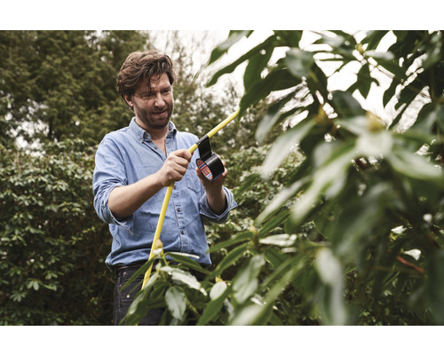 Mann repariert einen gelben Gartenschlauch mit Isolierband im Garten.