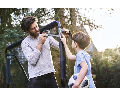 Vater und Sohn reparieren ein Fußballtor mit Klebeband im Garten.