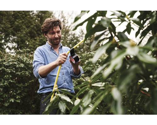 Ein Mann repariert einen gelben Gartenschlauch mit Isolierband im Garten.