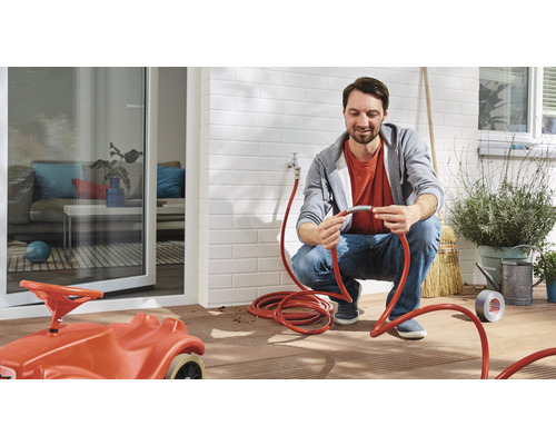 Ein Mann schließt einen Gartenschlauch an einen Wasserhahn im Außenbereich an.