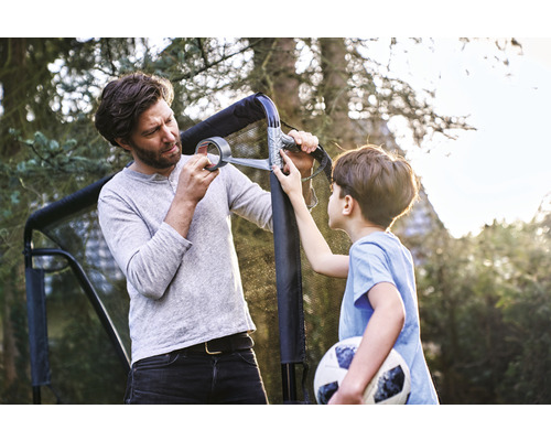 Vater und Sohn reparieren ein Fussballtor mit Klebeband im Garten.