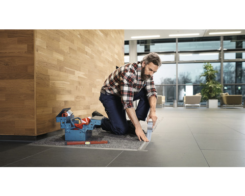 Handwerker kniet mit Werkzeugkasten und Klebeband auf dem Boden