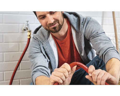 Mann hält einen undichten Wasserschlauch fest.