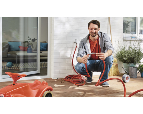 Mann verbindet einen Gartenschlauch im Außenbereich, mit Kinderspielzeugauto im Vordergrund