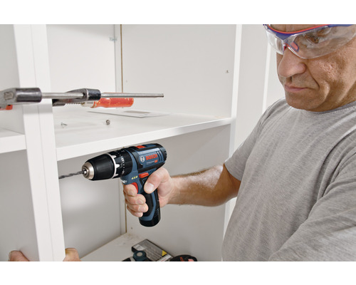 Ein Mann bohrt mit einem Akku-Bohrschrauber in ein weißes Regal