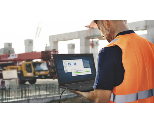 Bauarbeiter mit Laptop auf einer Baustelle mit Kran