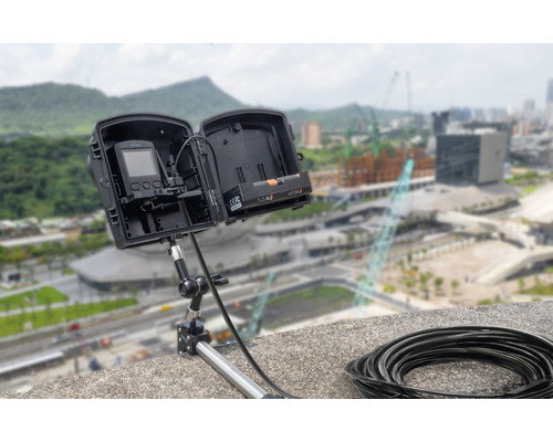 Zeitraffer Kamera mit Gehäuse auf einem Stativ montiert, im Hintergrund Stadtansicht