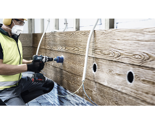 Ein Mann bohrt mit einer Bohrmaschine ein Loch in eine Holzwand für die Installation von Rohren