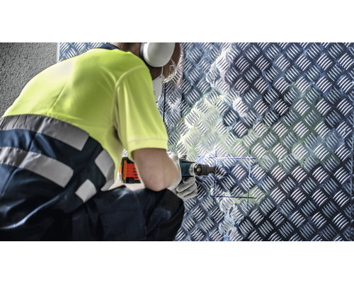 Handwerker bohrt mit einem Multifunktionswerkzeug in eine Riffelblechwand