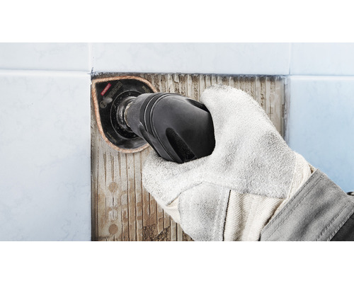 Hand mit Schutzhandschuh entfernt Fliesen mit einem Multitool