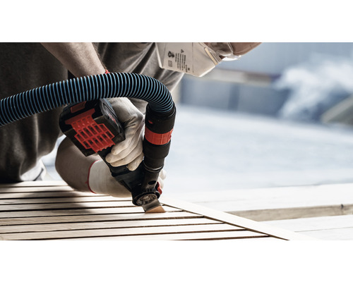 Person schleift Holz mit einem Elektrowerkzeug mit Staubsaugeranschluss, Schutzmaske und Handschuhen