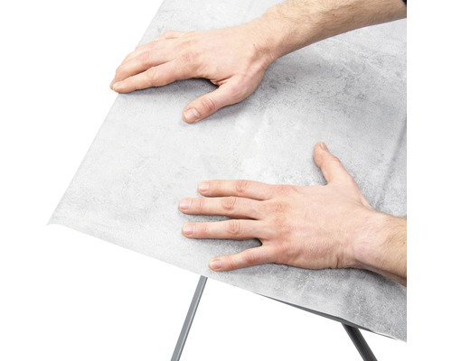 Mann befestigt Möbelfolie auf einer Oberfläche.