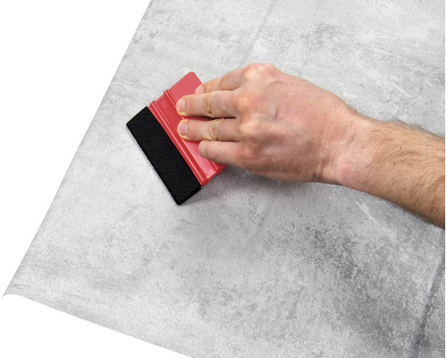 Hand mit Rakel beim Anbringen einer Folie mit Steinmuster