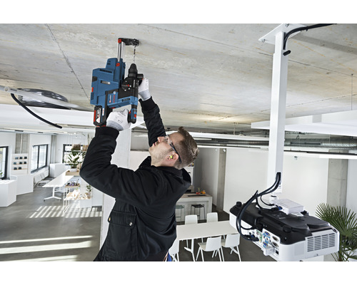 Ein Mann bohrt mit einer Schlagbohrmaschine ein Loch in die Decke in einem hellen Raum.