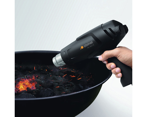 Eine Hand hält ein Steinel HL 1821 S Heißluftgebläse über einem Holzkohlegrill.