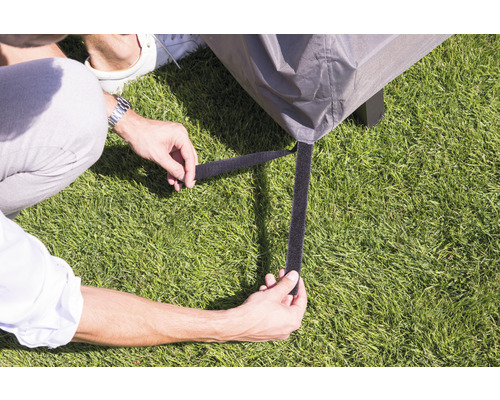 Person befestigt Schutzhülle mit Klettverschluss an einem Gartentisch