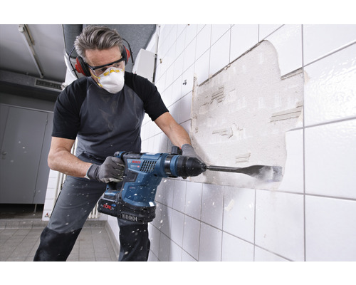 Mann mit Schutzbrille und Mundschutz arbeitet mit einem Abbruchhammer an einer gefliesten Wand