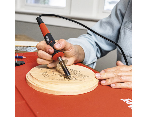 Person verwendet Brennkolben auf Holzscheibe